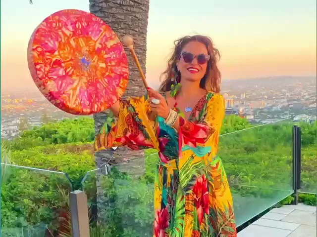 Vanessa Falabella holding a painted frame drum on a terrace at sunset